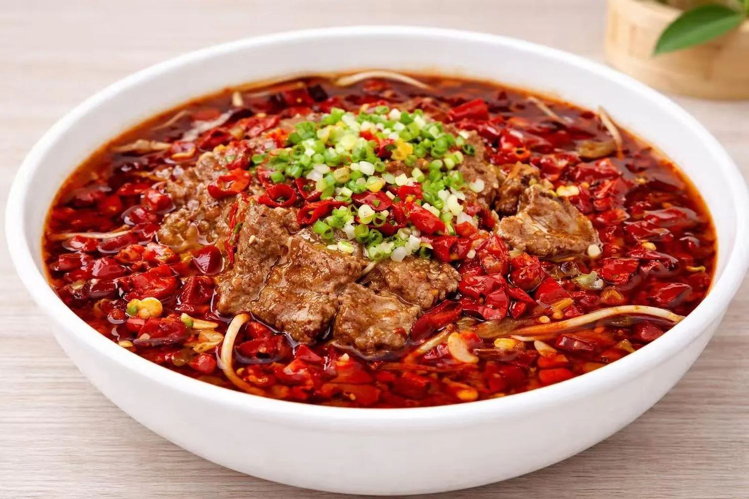 Boiled beef in spicy red chili oil with dried chilies and scallions in a white bowl