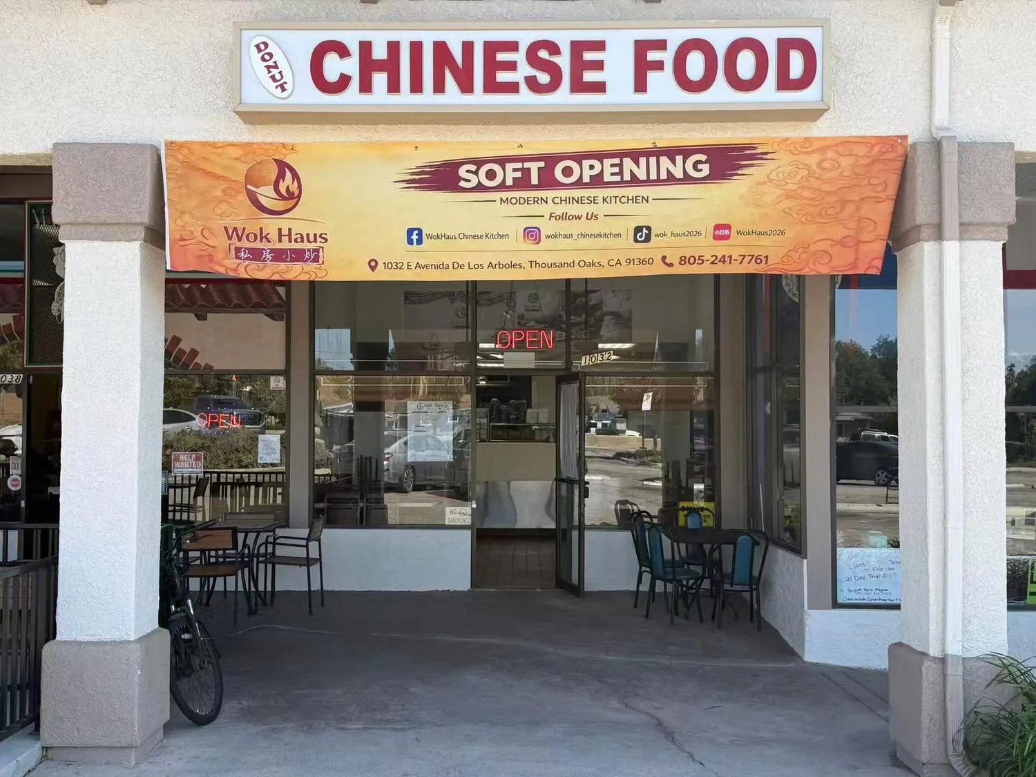 Storefront of Wok Haus Chinese restaurant with a soft opening banner and outdoor seating.